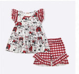 A toddler girl's two-piece summer outfit set featuring a white tiered dress with red and black barn and tractor prints, and matching red and white gingham ruffle shorts.