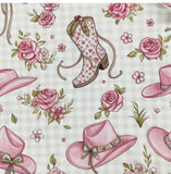 Pattern of pink cowboy hats and floral boots on a fabric background with pink roses.