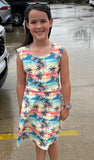 Young girl wearing a colorful dress with palm tree pattern on a wet pavement background. Sunset Oasis Athletic Girls Dress