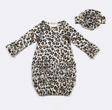 A baby girl's long-sleeve romper with a leopard print pattern, featuring ruffled cuffs and a ruffled hem, shown alongside a matching headband on a light gray background.