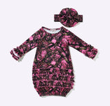 A toddler girl's long-sleeve ruffle dress in a pink and black camouflage print, shown with a matching fabric headband on a light gray background.