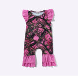 A toddler's short-sleeve romper with a bright pink background and a black branch camouflage pattern, featuring ruffled cap sleeves and ruffled leg cuffs, shown flat on a light gray background.