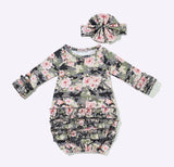 A baby long-sleeve romper with a ruffled hem and a matching fabric headband, both featuring a floral print over a dark camouflage base. The print includes pink and light green flowers on a black and gray camo pattern, displayed flat against a light gray background.