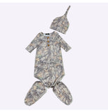 A baby three-piece outfit set featuring a short-sleeve footed onesie, matching booties, and a knit hat, all in a realistic woodland camouflage pattern with brown buttons on the chest.