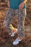 Person wearing zebra print pants and white sneakers in a dry grass field
