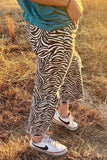Person wearing zebra print pants and white sneakers with black swooshes in a grassy field.