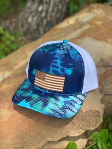Kryptek blue hat with American flag leather patch on crown sitting on a rock