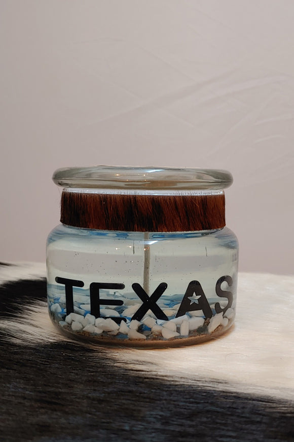 Gel candle with the word Texas cutout of metal set inside the gel. photographed on a cowhide.