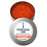 A small, round tin Fredericksburg Farms air freshener with a orange solid color interior, labeled 'Fredericksburg Juicy Peach'.