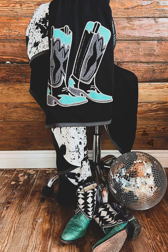 Walk it Out blanket by 2 Fly Co draped over a rolling chair with turquoise and black cowboy boots and a disco ball on the floor. Wooden background