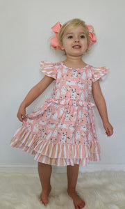 Ruffled dress with bunnies and flowers. Background of dress is peach. Ruffled short sleeves.