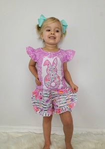 Toddler girl wearing purple splatter top with ruffle shirt sleeves and bunny on front. Striped shorts with floral print (front)
