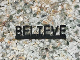 A metal cutout of the word believe for the Branding Stove candle