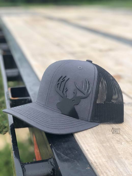 Smokey grey and black trucker hat with a black metal buck cutout on the crown